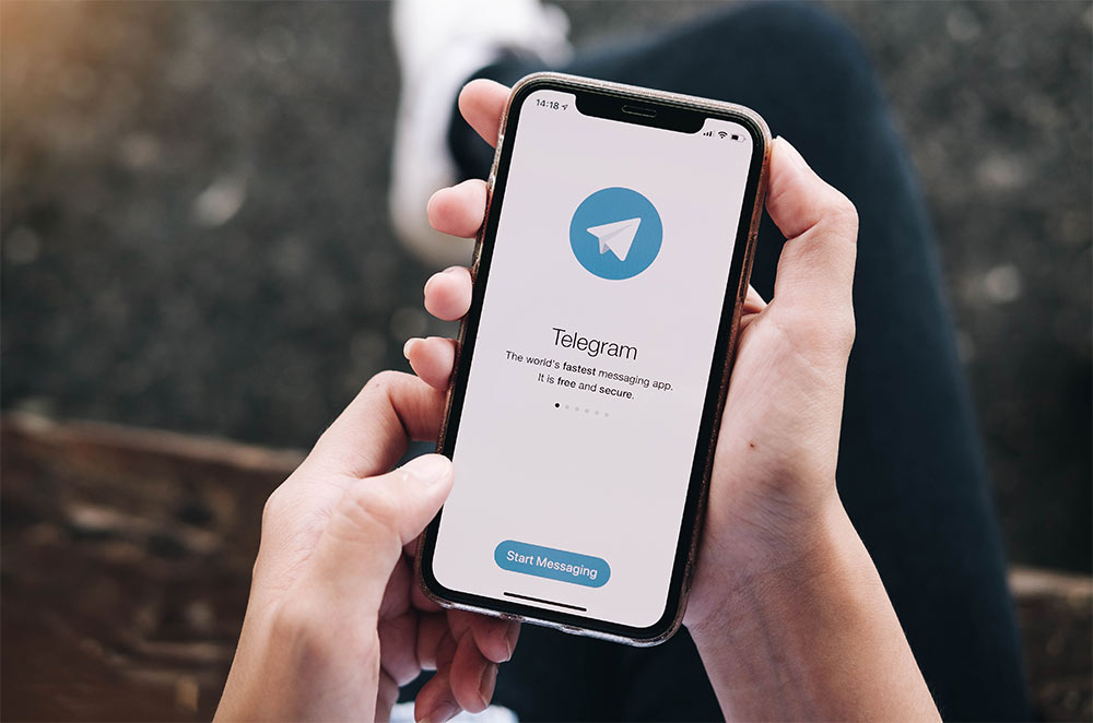 Person mit Smartphone in der Hand, wo die App Telegram geöffnet wurde.